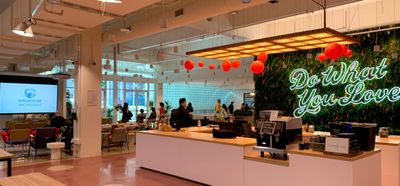 A view of the WeWork SF office, with an artificial plant wall with “Do What You Love” lit in neon, and the World IA Day 2020 San Francisco logo on one of the large projector screens.