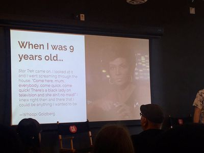 A man presents a slide with a quote from Black actress Whoopi Goldberg talking about seeing fellow Black actress Nichelle Nichols playing Uhura on Star Trek, and being inspired. 