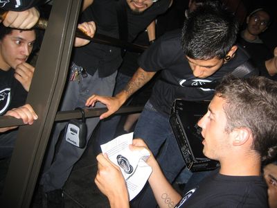 A group of young men wearing Batman-themed t-shirts excitedly crowd around one man reading a note from a lockbox with a Citizens for Batman stamp on it.